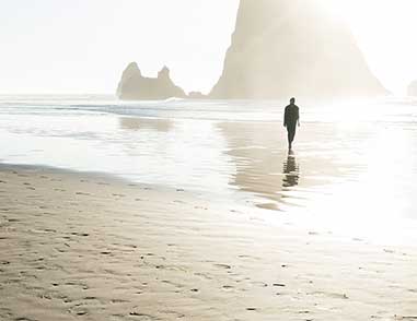 Человек идет по пляжу, на фоне две скалы